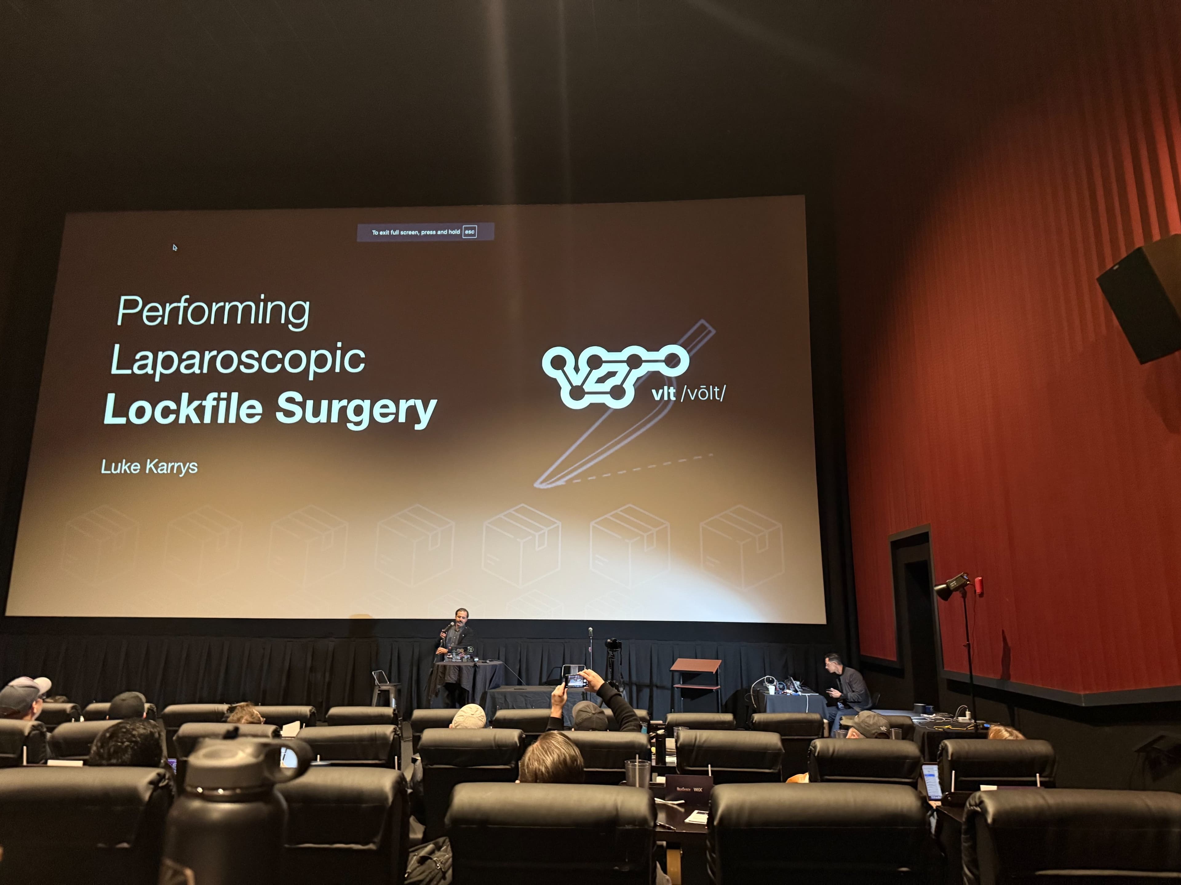 Me standing at the front of a movie theater with a slide on the screen that reads "Performing Laparoscopic Lockfile Surgery"